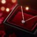 Red heart necklace in open red velvet jewelry box, displayed against backdrop of blurred rose petals and warm glowing lights