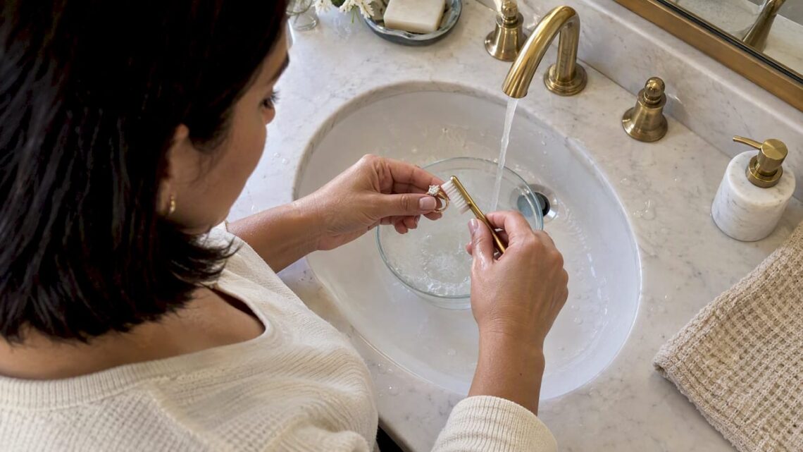 Hands gently cleaning a diamond ring at home