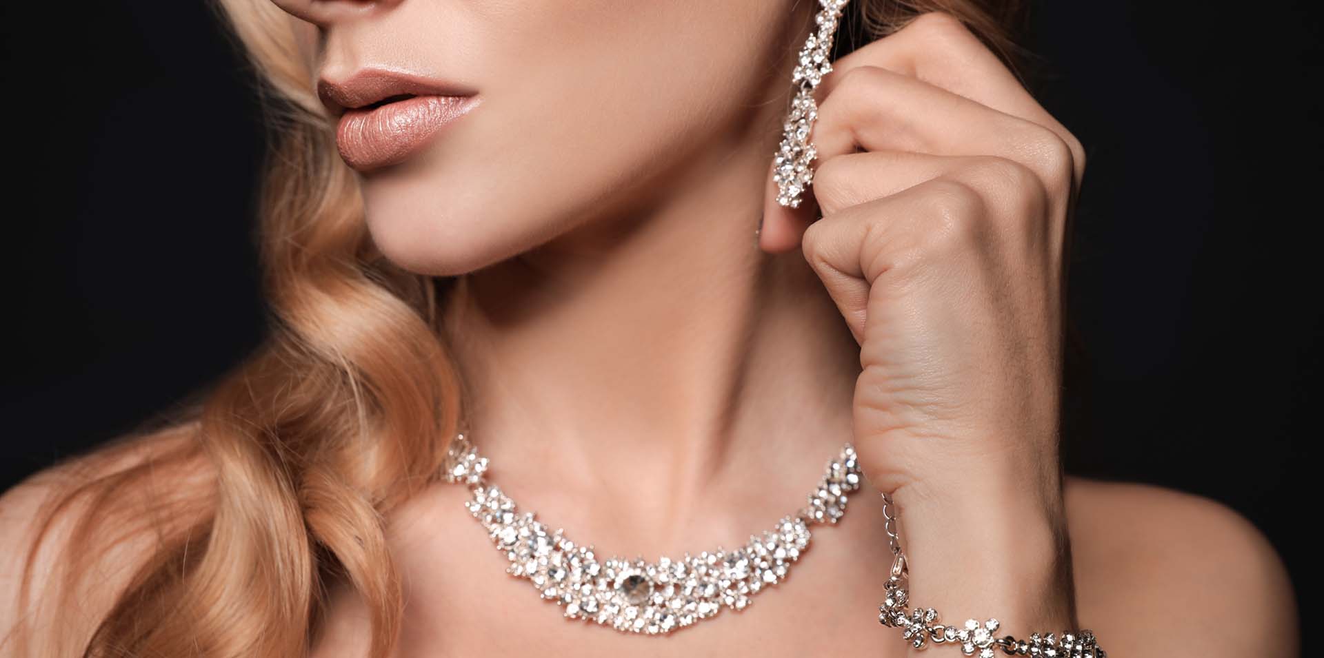 A closeup of a woman modeling diamond jewelry. Hanging diamond earrings, a diamond necklace and a diamond bracelet: Telephone number 1-877-872-9909