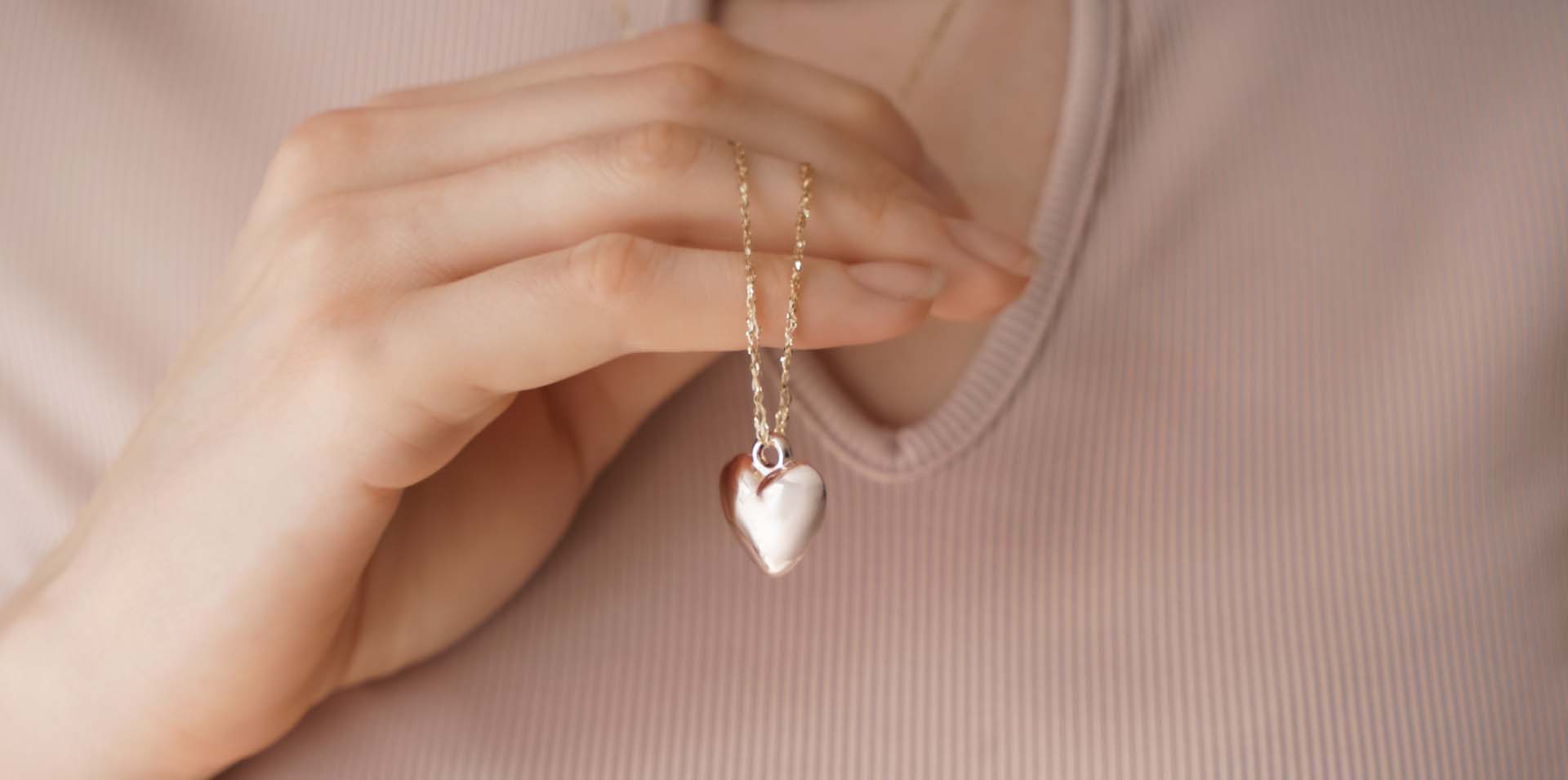 Closeup of woman displaying a gold heart necklace: Telephone number 1-877-872-9909
